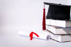 Kitap yığını üzerindeki mezuniyet kepi ve kırmızı kurdeleli diploma – yurt dışı denklik başvurusu ve STS sınavı iptal davası.