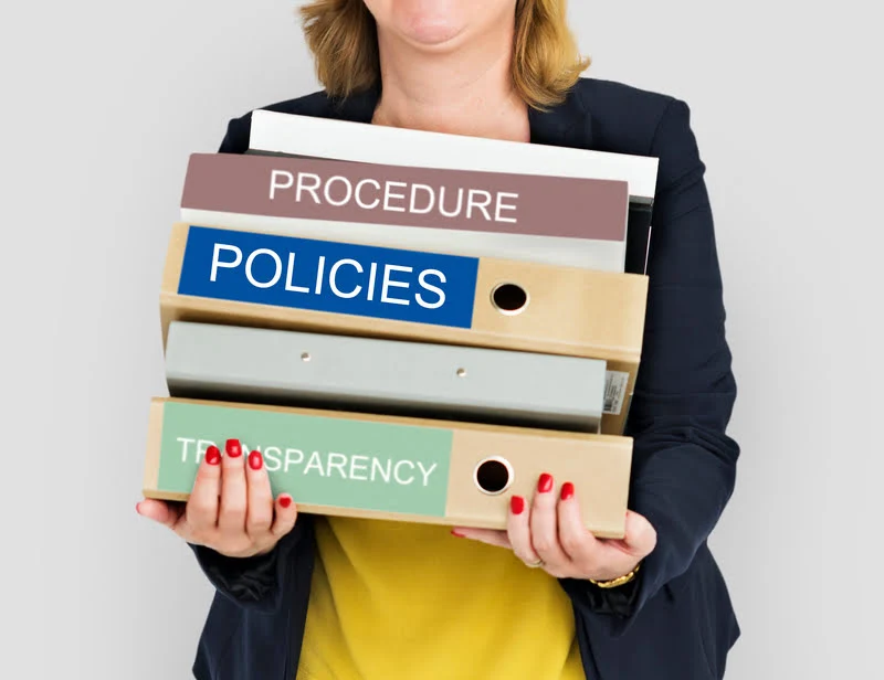 Bir profesyonelin elinde "PROCEDURE", "POLICIES" ve "TRANSPARENCY" etiketli dosya klasörlerini tuttuğu, kurumsal yönetim ve hukuki uyum süreçlerini temsil eden görsel.